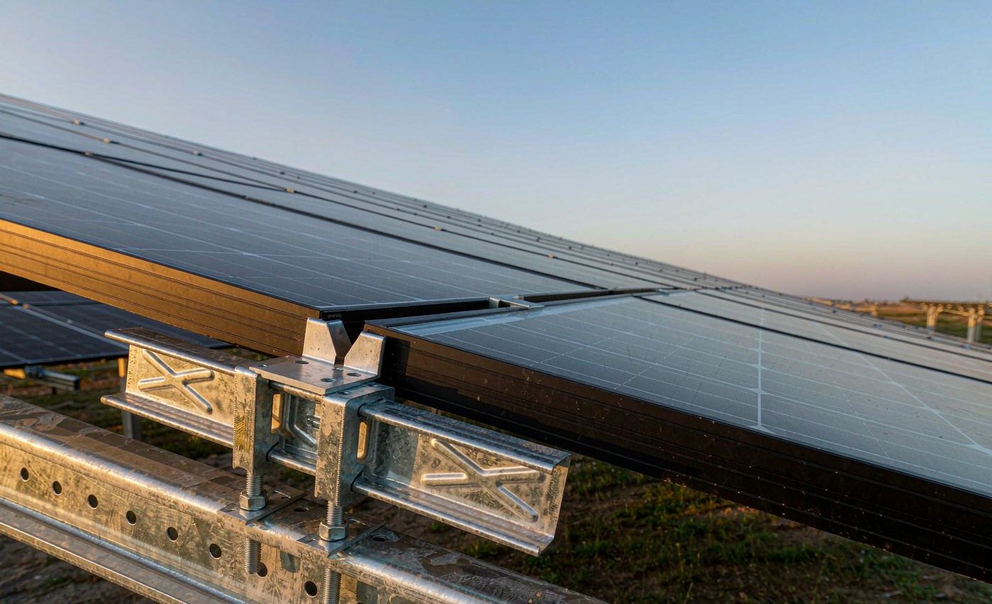 Steel middle clamp fastening solar panel frames onto a galvanized C-channel rail at a solar farm